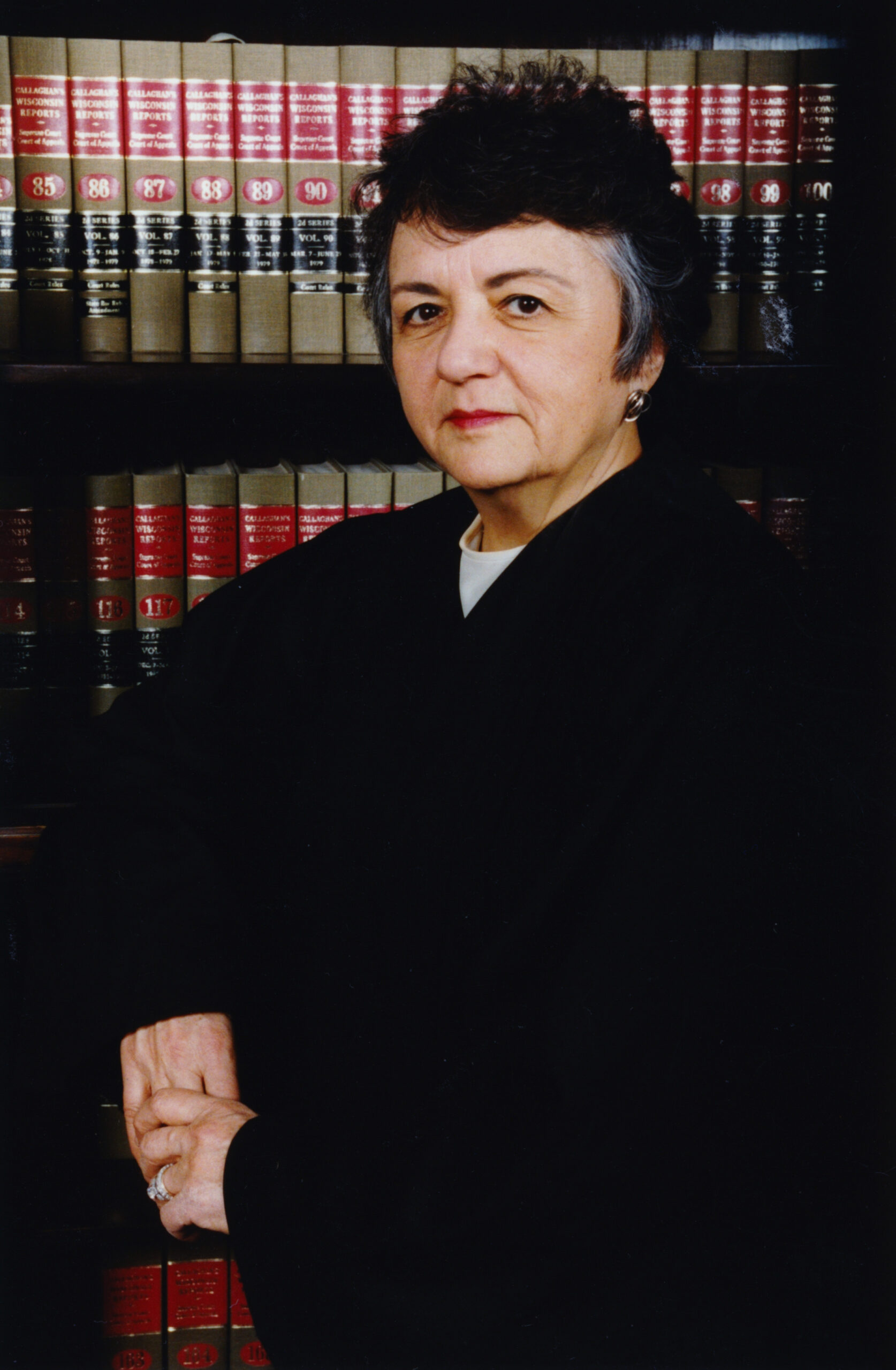 Justice Abrahamson wearing her judicial robes, standing in front of shelves full of law books.